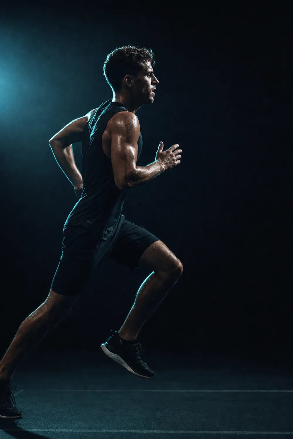 Athlete mid-stride in a dark training space, lit from the side